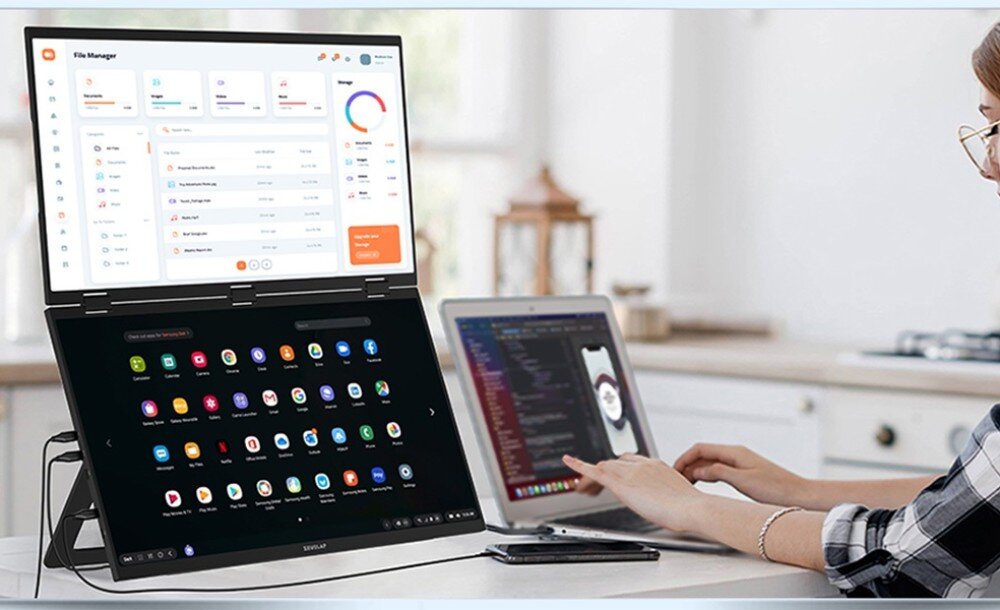 Monitor ZEUSLAP Z18W Kobieta siedząca przy stole pracuje na laptopie, obok którego stoi składany monitor z dwoma ekranami wyświetlającymi różne aplikacje, opis