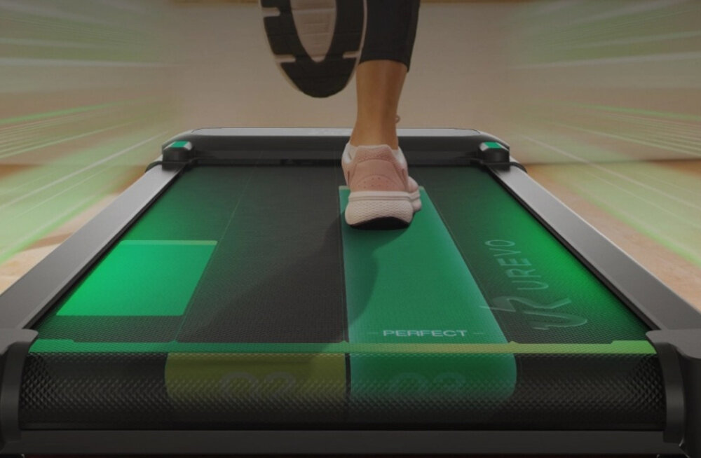 Bieżnia elektryczna UREVO Spacewalk 5 600W 6 km-h pomieszczenie osoba biegnie na bieżni zbliżenie na pas biegowy pas bieżny o wymiarach 40 × 100 cm odpowiednia przestrzeń do swobodnego kroku naturalna postawa stabilność ruchu wspiera dłuższe i bardziej komfortowe sesje treningowe