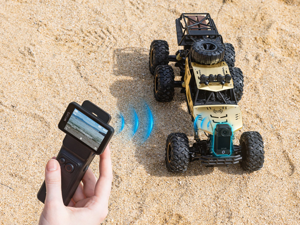 SJCAM C400 Wbudowane moduły Wi-Fi i Bluetooth zdalne sterowanie podgląd obrazu na żywo Uchwyt z wbudowanym pilotem transmisje na żywo tryb webcam - kamera a w tle samochód zdalnie sterowany na piasku