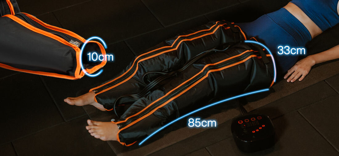Osoba leży na macie, mając na nogach czarne urządzenie z pomarańczowymi akcentami, podłączone do panelu sterującego. Widoczne są wymiary: 10 cm, 33 cm i 85 cm.
