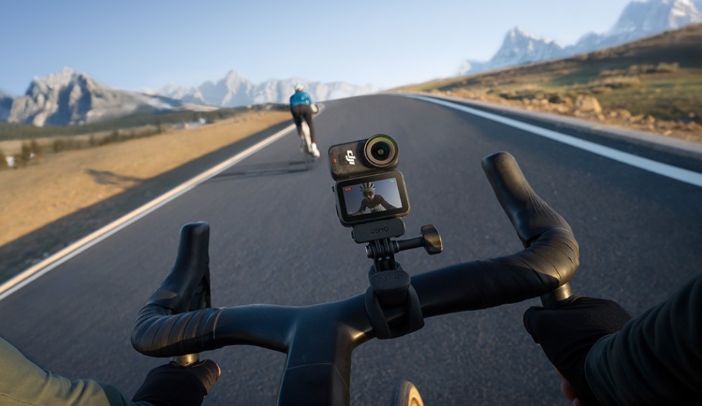 Kamera sportowa DJI Osmo Nano Widok z perspektywy rowerzysty trzymającego kierownicę, na której zamontowana jest kamera, przed nim drugi rowerzysta na górskiej drodze, wodoodporność, norma IPX4
