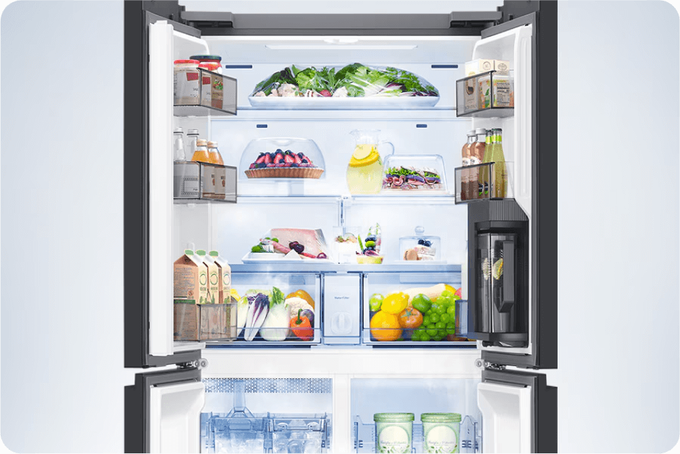 Otwarta lodówka z wypełnionymi półkami. Widać warzywa, owoce, soki, napoje w butelkach, nabiał oraz mięso.