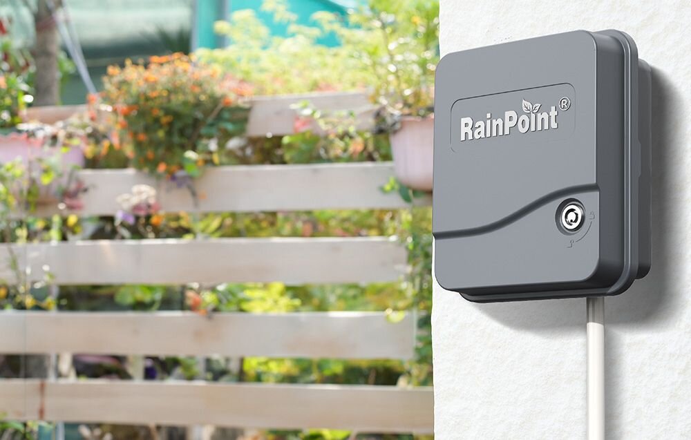 Sterownik nawadniania RAINPOINT ITC1200, sterownik nawadniania, wiele stref, ogród, kontrola, Zamknięty sterownik nawadniania RainPoint zamontowany na ścianie obok rośli.