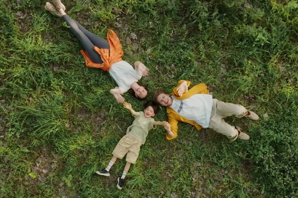 Dron HOVERAIR X1 Combo Plus Widok z góry na trzy osoby leżące na trawie i machające do kamery