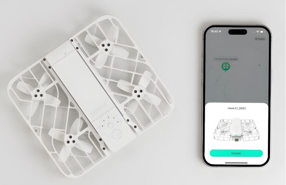 Dron HOVERAIR X1 Combo Plus Złożony biały dron leżący obok smartfona z włączoną aplikacją