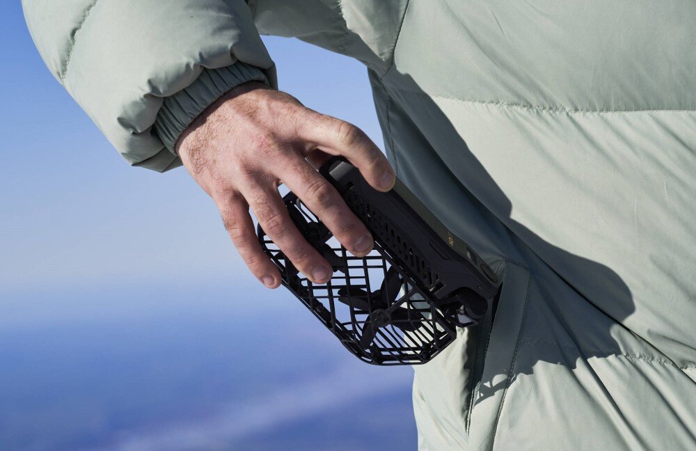 Dron HOVERAIR X1 Pro Basic Combo Dłoń trzymająca złożony czarny dron przy kieszeni jasnej puchowej kurtki, cechy, waga