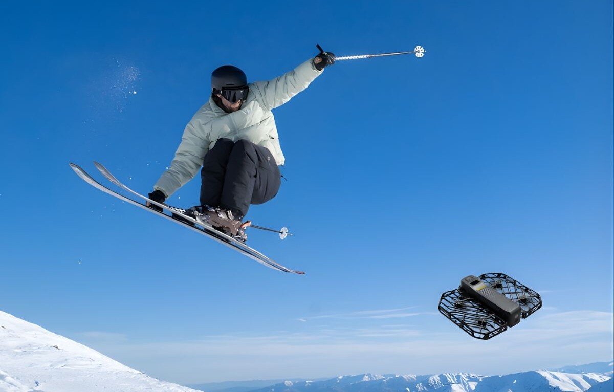 Dron HOVERAIR X1 Pro Basic Combo Narciarz wykonujący skok w powietrzu na tle nieba z unoszącym się obok czarnym dronem, bateria, czas lotu