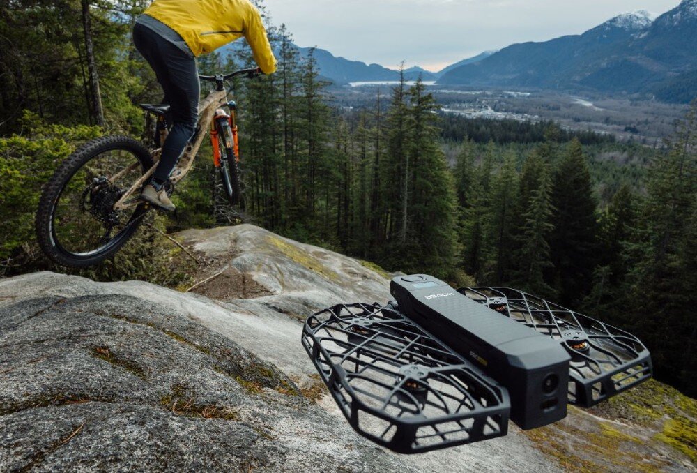 Dron HOVERAIR X1 Pro Ultimate Cycling Kit Narciarz wykonujący skok w powietrzu na tle nieba z unoszącym się obok czarnym dronem, bateria, czas lotu