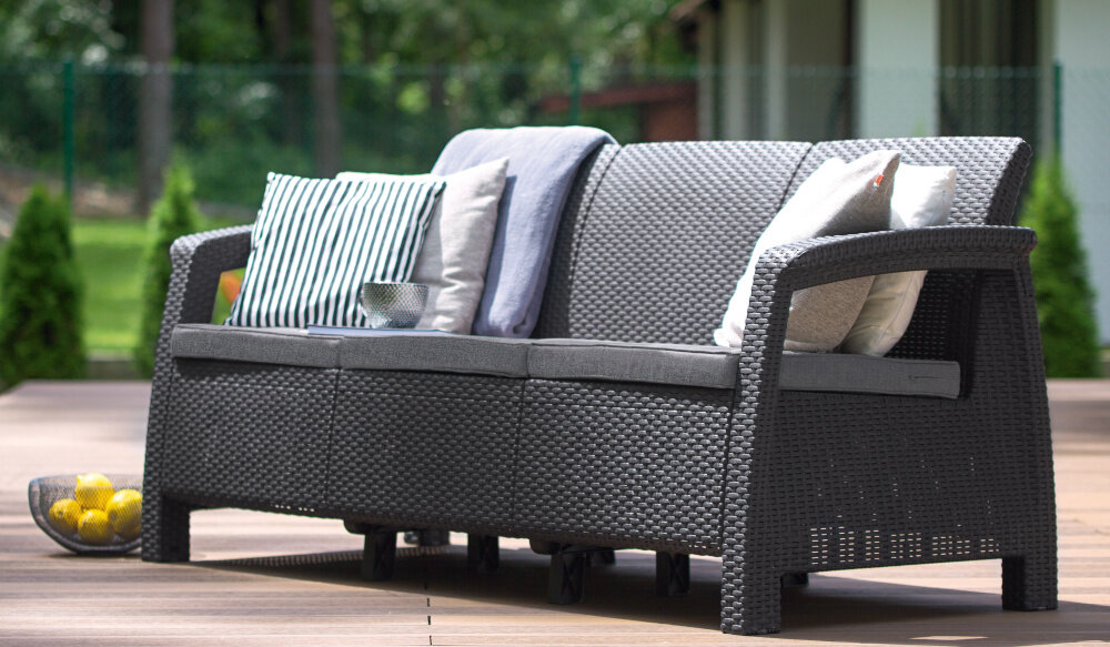 Sofa ogrodowa KETER Cofru Love Seat 3 osobowa Grafitowy sofa na tarasie w tle rośliny i dom odpoczynek na świeżym powietrzu miłe chwile w gronie rodzinnym lub z przyjaciółmi komfort relaks