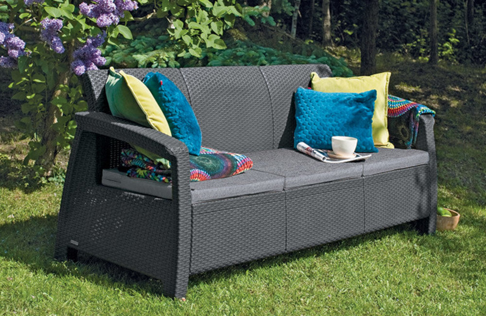 Sofa ogrodowa KETER Cofru Love Seat 3 osobowa Grafitowy sofa na trawie w tle drzewa i rośliny niewielkie rozmiary 182 x 70 x 79 cm odpoczynek na świeżym powietrzu obciążenie do 330 kg