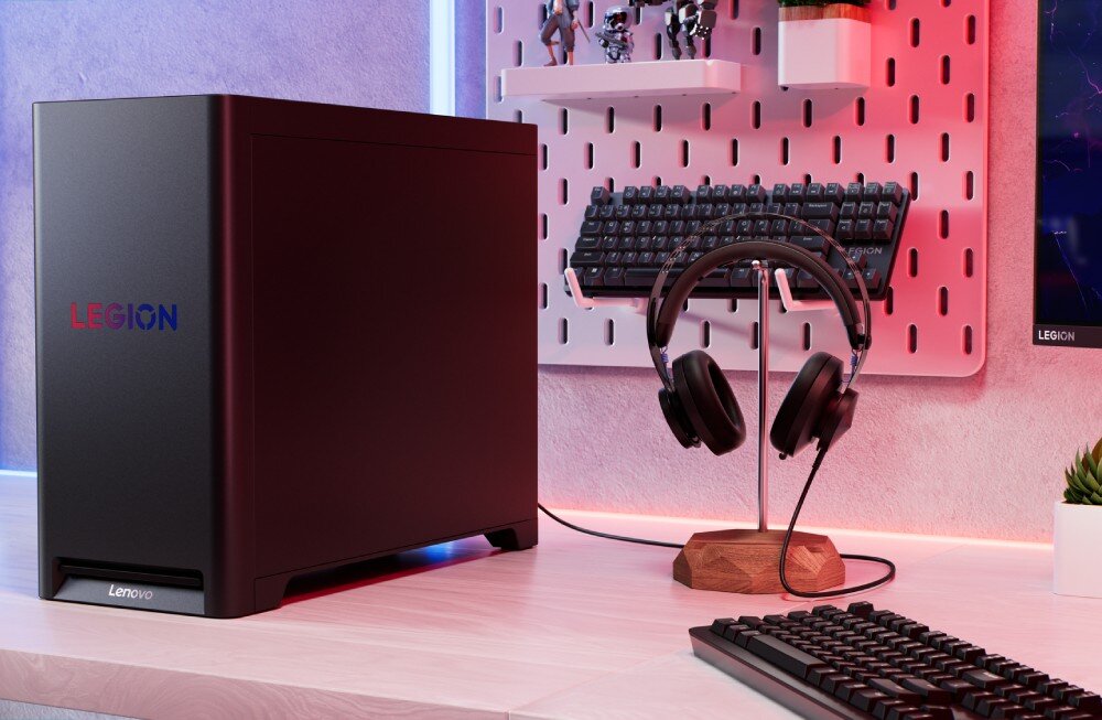 Komputer LENOVO Legion T5 30AGB10 Komputer ustawiony na biurku, widok od boku na czarną obudowę z logo 'LEGION', obok stojak ze słuchawkami i klawiatura na ścianie