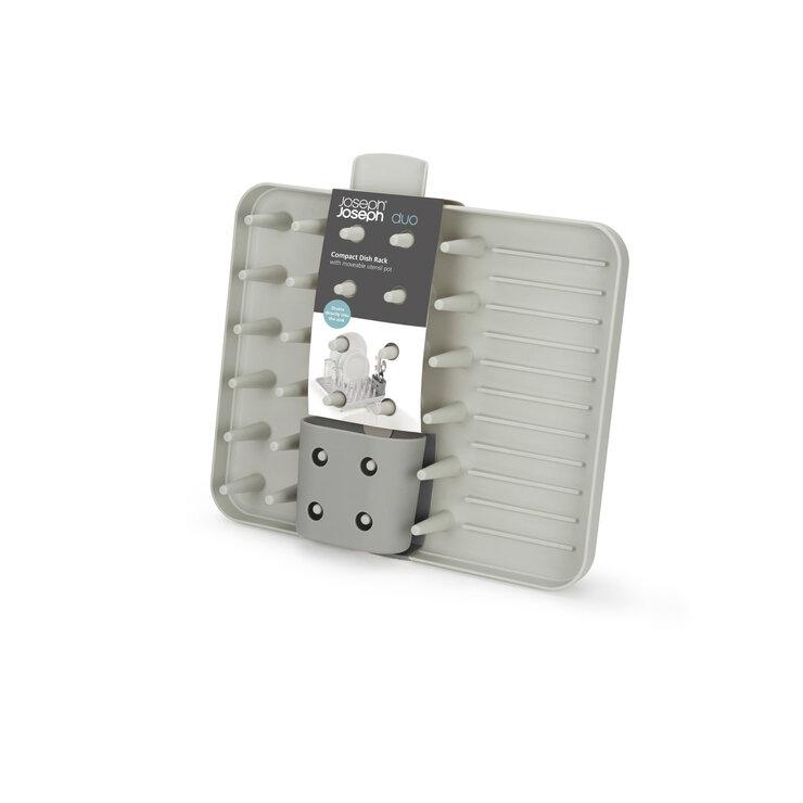 Szara suszarka do naczyń z odpływem, posiadająca pionowe pręty do podtrzymywania naczyń oraz miejsce na sztućce. Na produkcie widoczny jest tekst: \'Joseph Joseph duo Compact Dish Rack with removable utensil pot\'.