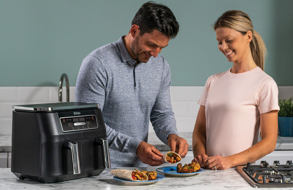 Air Fryer Frytkownica beztłuszczowa NINJA AF200EU z podwójnym koszem kuchenne tło kobieta mężczyzna frytkownica przyciski dwa kosze mężczyzna układający tortillę na talerzu dwustrefowa moc 2400 W 38 x 31 x 33 cm wygodne i efektywne gotowanie dwie różne potrawy na dwa sposoby zsynchronizuje czas ich zakończenia 4 automatyczne programy: smażenie beztłuszczowe, MAX Crisp, pieczenie i odgrzewanie ręczne dostosowanie ustawień wiele możliwości kulinarnych dla par i rodzin w każdej kuchni