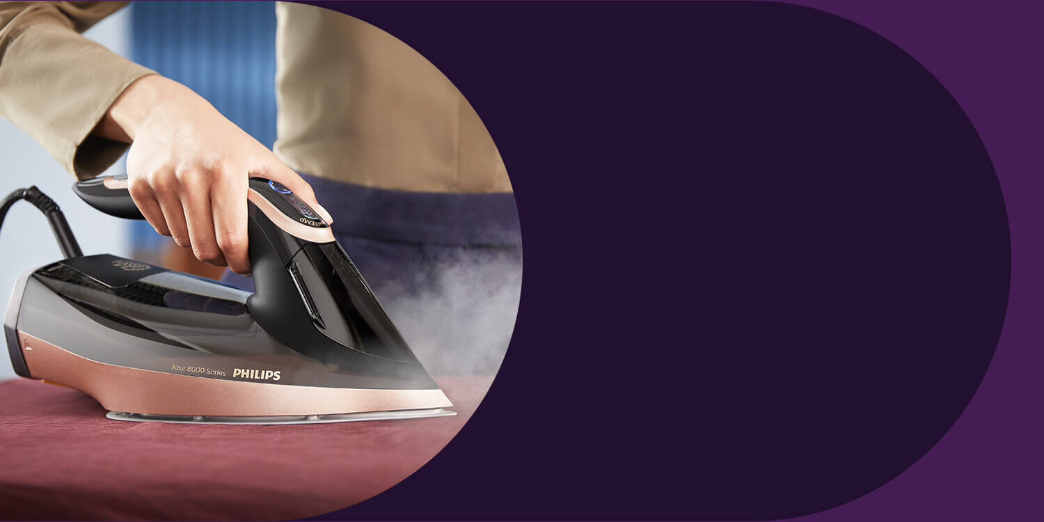 Osoba prasuje tkaninę żelazkiem marki PHILIPS, model Azur 8000 Series. Żelazko emituje parę podczas prasowania.