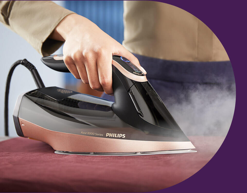 Osoba prasuje tkaninę żelazkiem z napisem \'Azur 8000 Series PHILIPS\'. Żelazko emituje parę podczas prasowania.
