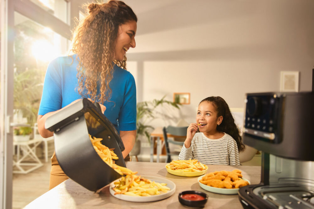 Air Fryer Frytkownica beztłuszczowa BRAUN MultiFry 5 HF5073 uśmiechająca się kobieta i dziecko kobieta w ręku trzyma kosz, z którego wysypuje frytki na talerz z 20 automatycznymi programami gotowania pieczenie, grillowanie i smażenie technologia RealOven Tec 3w1 równomierna dystrybucja ciepła szybkie i optymalne rezultaty chrupiące frytki soczyste mięsa pieczone warzywa desery 20 automatycznych programów łatwe gotowanie pojemna szuflada 6 l dla całej rodziny 