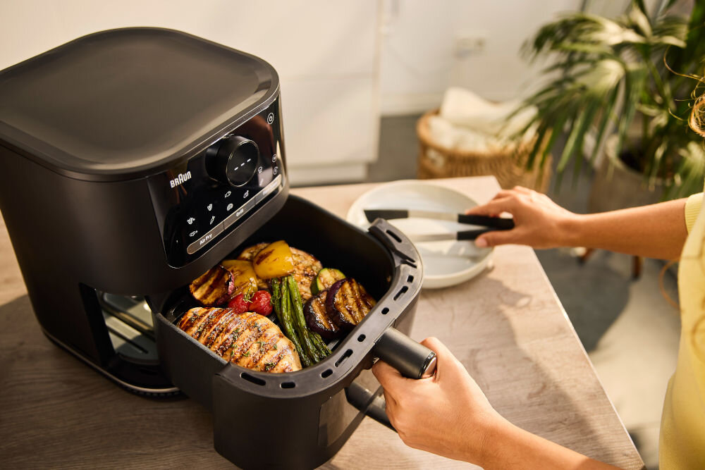 Air Fryer Frytkownica beztłuszczowa BRAUN MultiFry 5 HF5073 frytkownica czarna obudowa przyciski panel wyświetlacz osoba wyciąga kosz, w którym znajduje się potrawa  z 20 automatycznymi programami gotowania moc 2000 W stałe silne dostarczenie temperatury optymalne efekty kulinarne kompaktowe rozmiary wydajność ulubione dania ułatwienie codziennego gotowania dobre rezultaty 