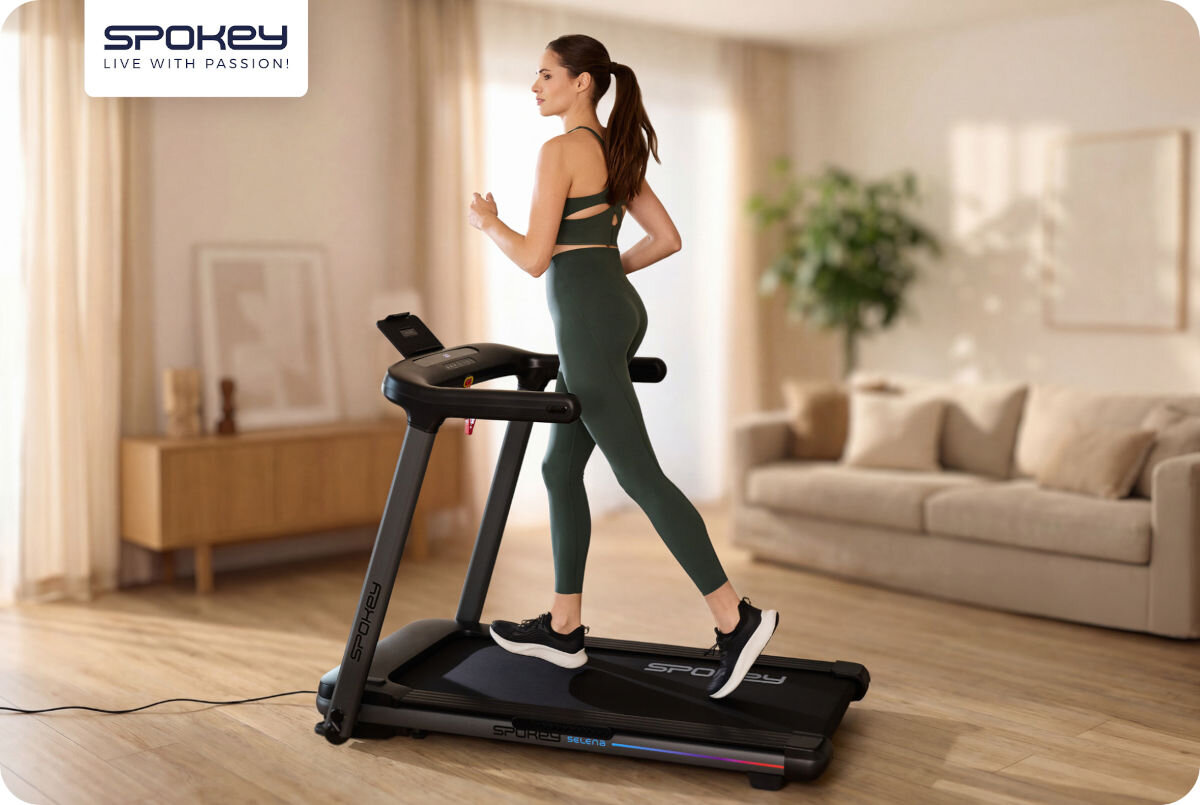 Bieżnia elektryczna SPOKEY Selena 1305W 14 km/h, motywacja, kondycja, trening, energia, Kobieta w legginsach biega na składanej bieżni Spokey LEAN w salonie.
