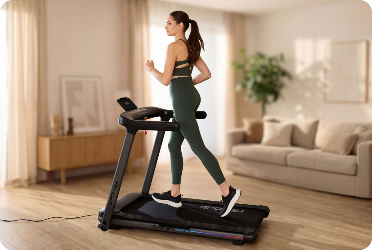 Bieżnia elektryczna SPOKEY Selena 1305W 14 km/h, motywacja, kondycja, trening, energia, Kobieta w legginsach biega na składanej bieżni Spokey LEAN w salonie.