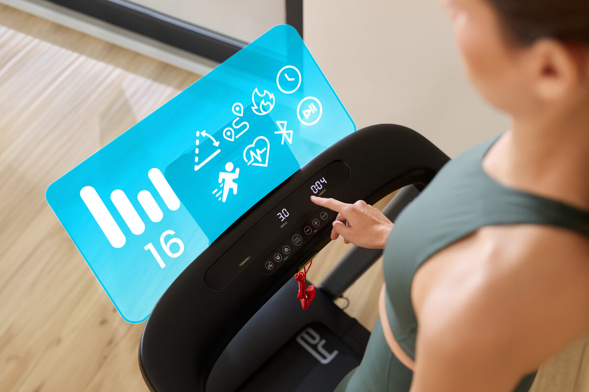 Bieżnia elektryczna SPOKEY Selena 1305W 14 km/h, różnorodność, cele, dynamika, efektywność, Kobieta dotyka wyświetlacza bieżni Spokey LEAN z hologramem funkcji 16km/h.