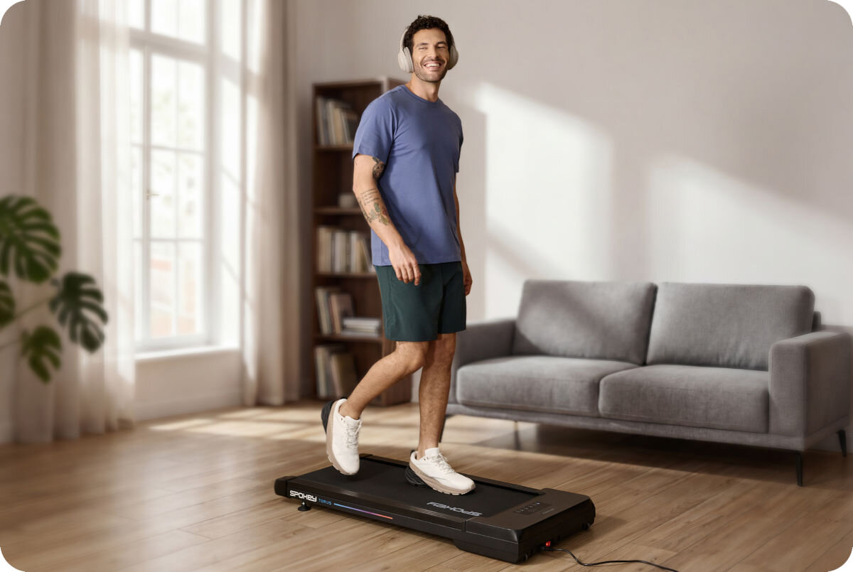 Bieżnia elektryczna SPOKEY Torus 946145 745.7W 6 km/h, aktywność, zdrowie, trening, komfort, Mężczyzna w szortach i sneakersach maszeruje na bieżni Spokey WALK pod oknem.