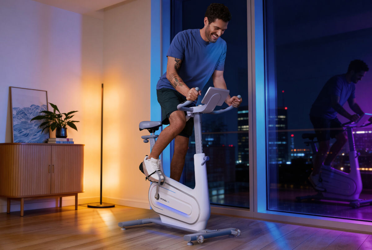 Rower elektromagnetyczny SPOKEY Zen, płynność, stabilność, balans, ruch, Mężczyzna trenuje na rowerze Spokey wieczorem w mieszkaniu z widokiem na miasto.