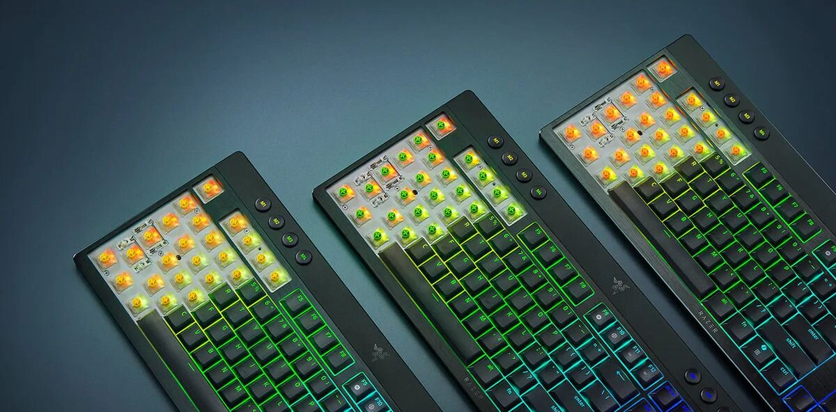 Na obrazie widoczne są trzy klawiatury z podświetleniem RGB, każda z nich ma różne kolory podświetlenia klawiszy. Na klawiaturach znajduje się logo Razer.