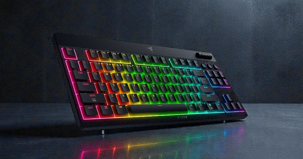 Klawiatura z podświetleniem RGB, z widocznym logo producenta na górze. Klawisze mają różne kolory, tworząc efekt tęczy.