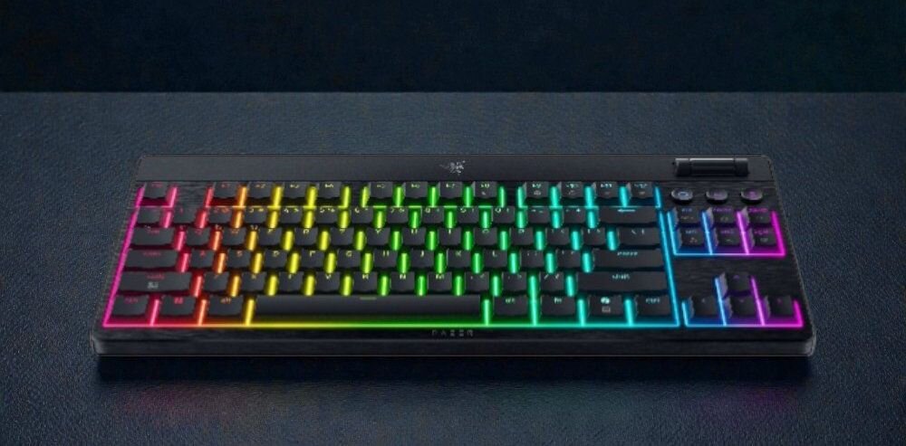 Klawiatura mechaniczna z podświetleniem RGB, widoczne logo producenta na górze. Klawisze mają różnokolorowe podświetlenie, a obudowa jest czarna.