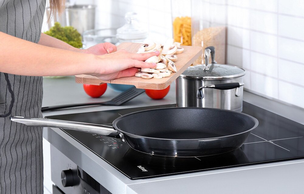 Płyta indukcyjna ISEASY LI4-20 Pokrojone pieczarki są zsuwane z deski do patelni ustawionej na płycie grzewczej. Obok stoi garnek z pokrywką i kuchenne akcesoria Child Lock wskaźnik ciepła automatyczne wyłączanie