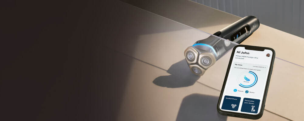 Oparty o ręcznik smartfon z włączoną aplikacją na monitorze. Obok golarka ze świecącym niebieskim ringiem.