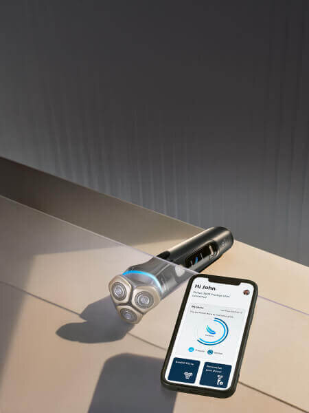 Oparty o ręcznik smartfon z włączoną aplikacją na monitorze. Obok golarka ze świecącym niebieskim ringiem.