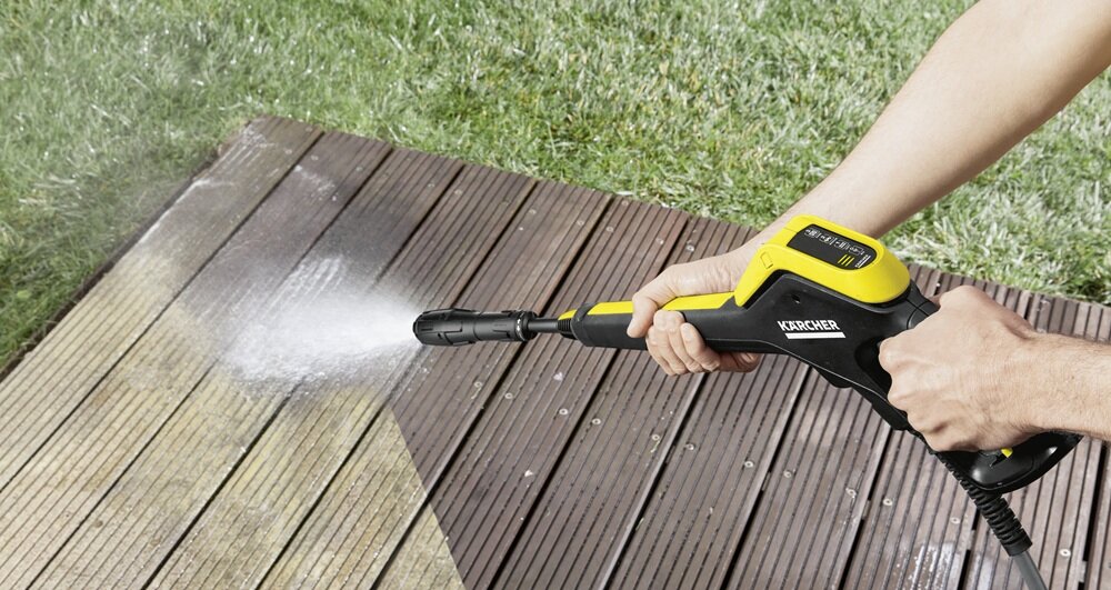 Osoba trzymająca myjkę ciśnieniową, która czyści drewnianą powierzchnię. Na urządzeniu widoczne jest logo \'KARCHER\'.