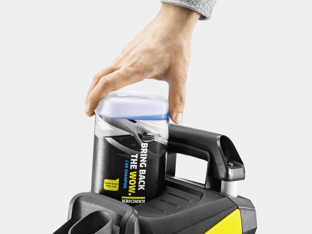 Ręka umieszcza pojemnik z napisem \'BRING BACK THE WOW! CAR SHAMPOO\' na urządzeniu z czarnym uchwytem i żółtym elementem. Widoczne jest logo \'KARCHER\'.