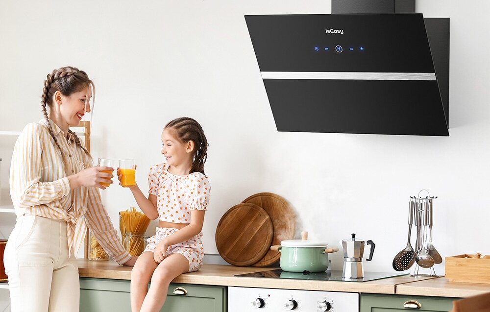 Okap kuchenny ISEASY TV5290D4-CC-I2 W kuchni dwie osoby piją sok przy blacie, a nad nimi pracuje czarny okap ścienny z podświetlanym panelem sterowania. Obok na płycie stoi garnek, z którego delikatnie unosi się para cichy okap 58 dB komfort