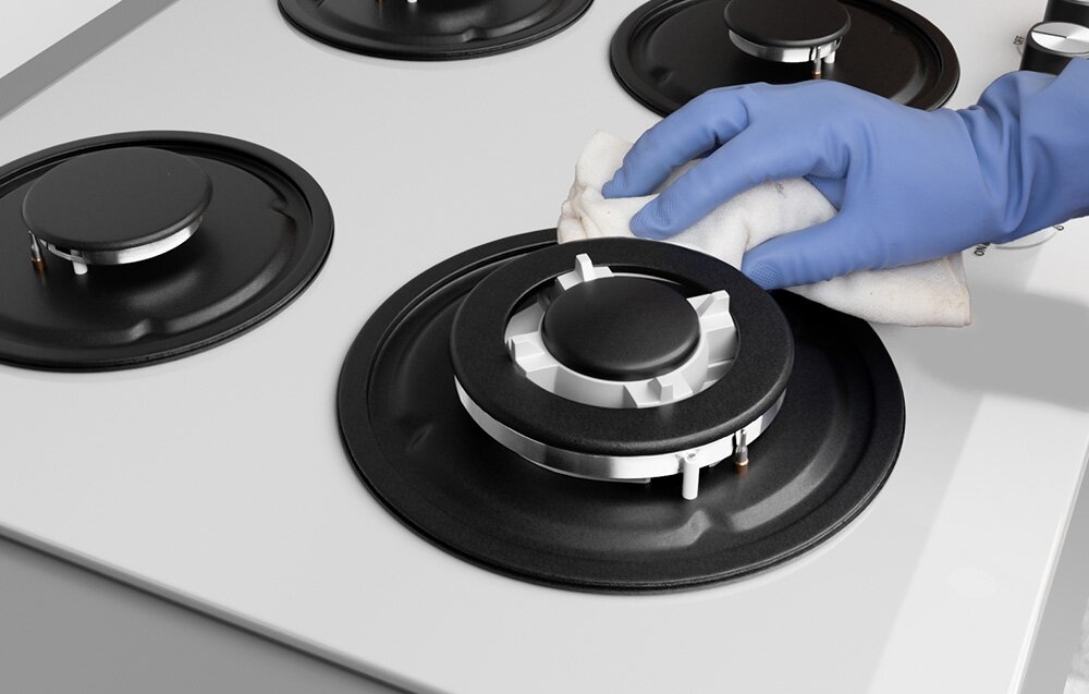 PŁYTA GAZOWA ISEASY MGBG-604B Ręka w rękawiczce czyści powierzchnię palnika miękką ściereczką. Widoczne są elementy metalowe i rozmieszczenie dysz grzewczych szkło hartowane 8mm żeliwne ruszty pokrętła bakelitowe odporność na zarysowania