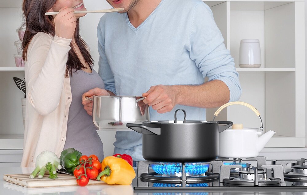 Płyta gazowa ISEASY MGBG-654A Dwie osoby gotują razem, podgrzewając potrawę w dużym garnku stojącym na środkowym palniku. Na blacie obok ułożono świeże warzywa i podstawowe produkty do przygotowania posiłku zabezpieczenie przeciwwypływowe czujnik płomienia automatyczne odcięcie gazu bezpieczne gotowanie