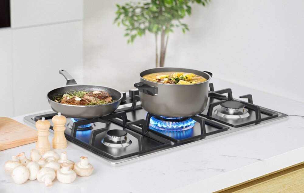 Płyta gazowa ISEASY MGBS-765 Na płycie gazowej stoją garnek z zupą oraz patelnia, z których unosi się para. Płomienie równomiernie ogrzewają naczynia ustawione na stabilnych rusztach pięć palników wysoka wydajność szybkie gotowanie kontrola płomienia