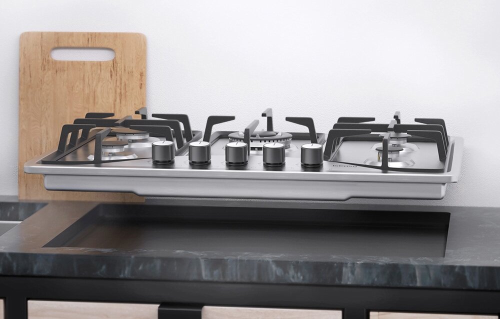 Płyta gazowa ISEASY MGBS-765 Zdjęcie ukazuje montaż płyty gazowej unoszonej nad blatem kuchennym. Widać całą konstrukcję urządzenia oraz system mocowania wymiary 76x50x9,5 cm montaż w blacie wnęka 73x48 cm elementy montażowe stabilna instalacja