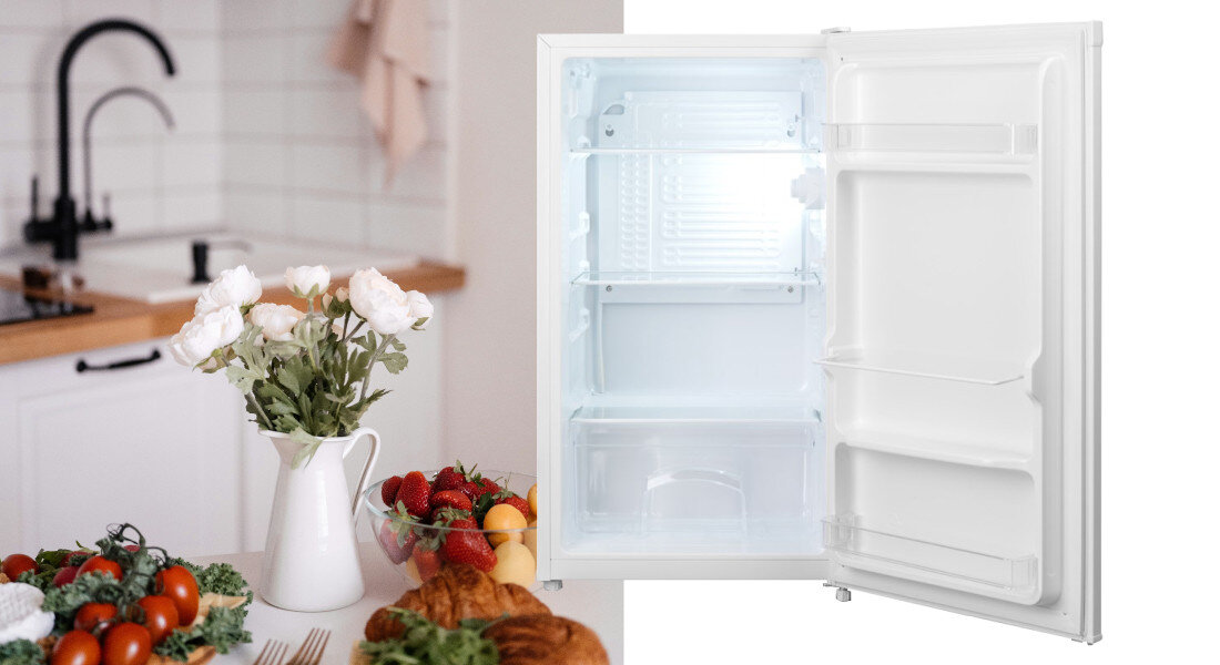 Lodówka GODDESS RME085GW8SSE Zdjęcie pokazuje otwartą, pustą lodówkę ustawioną w kuchni, obok stołu z pieczywem, owocami i kwiatami. Ujęcie podkreśla czyste wnętrze oraz funkcjonalny układ półek cicha praca 39 db niskie zużycie energia klasa e niskie rachunki oszczędności