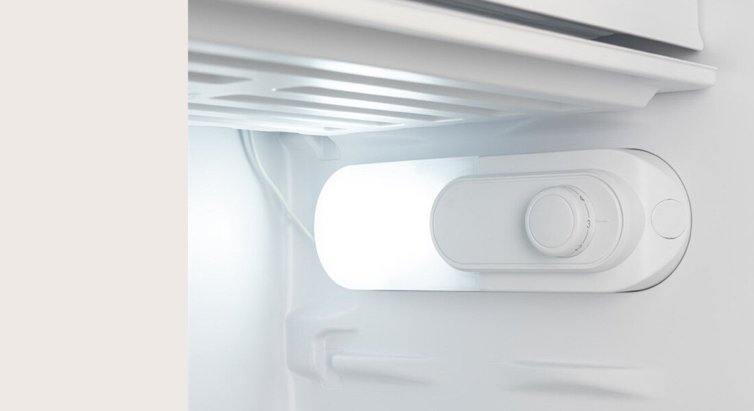 Lodówka GODDESS RME085GW8SSE Zdjęcie przedstawia zbliżenie na wnętrze lodówki z podświetleniem oraz mechanicznym pokrętłem regulacji temperatury. Detal pokazuje prostą i intuicyjną obsługę urządzenia sterowanie mechaniczne regulacja temperatury zmiana drzwi regulowane nóżki