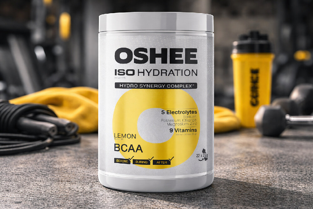Izotonik OSHEE Iso Hydration Cytrynowy (550 g) siłownia na podłodze stoi opakowanie izotoniku w tle bidon odpowiedni poziom nawodnienia waga 550 g 22 porcje napoju w opakowaniu lekka cytrynowa formuła orzeźwia i wspiera organizm