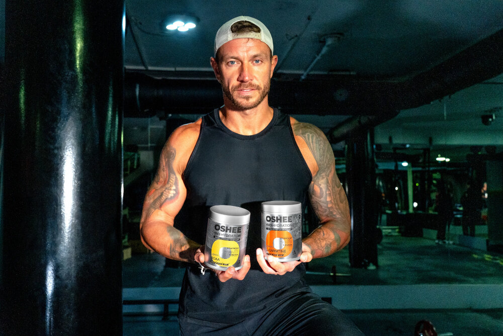 Izotonik OSHEE Iso Hydration Cytrynowy (550 g) siłownia osoba w stroju sportowym trzyma w dłoniach opakowania izotoników Hydro Synergy Complex™ zestaw elektrolitów wspierających gospodarkę wodno-elektrolitową organizmu cytrynian sodu cytrynian potasu chlorek potasu pomagają uzupełniać elektrolity tracone wraz z potem 340 kJ/80 kcal jednej porcji