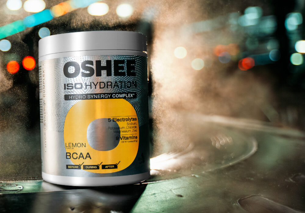 Izotonik OSHEE Iso Hydration Cytrynowy (550 g) ciemne tło opakowanie izotoniku dym woda aminokwasy rozgałęzione BCAA L-leucynę (400 mg) L-izoleucynę (200 mg) L-walinę (200&nbsp; mg) BCAA przypisuje się udział w procesach metabolicznych  praktyczne wsparcie codziennej aktywności fizycznej i regeneracyjnego stylu żywienia
