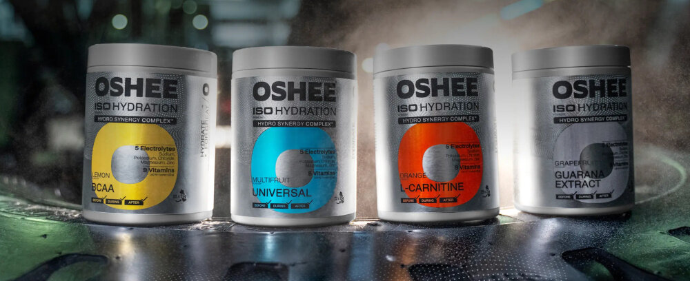 Izotonik OSHEE Iso Hydration Cytrynowy (550 g) cztery opakowania izotoników na ciemnym tle dym witamina C w postaci kwasu L-askorbinowego w ilości 320 mg wspiera prawidłowe funkcjonowanie układu odpornościowego pomaga chronić komórki przed stresem oksydacyjnym witamina C