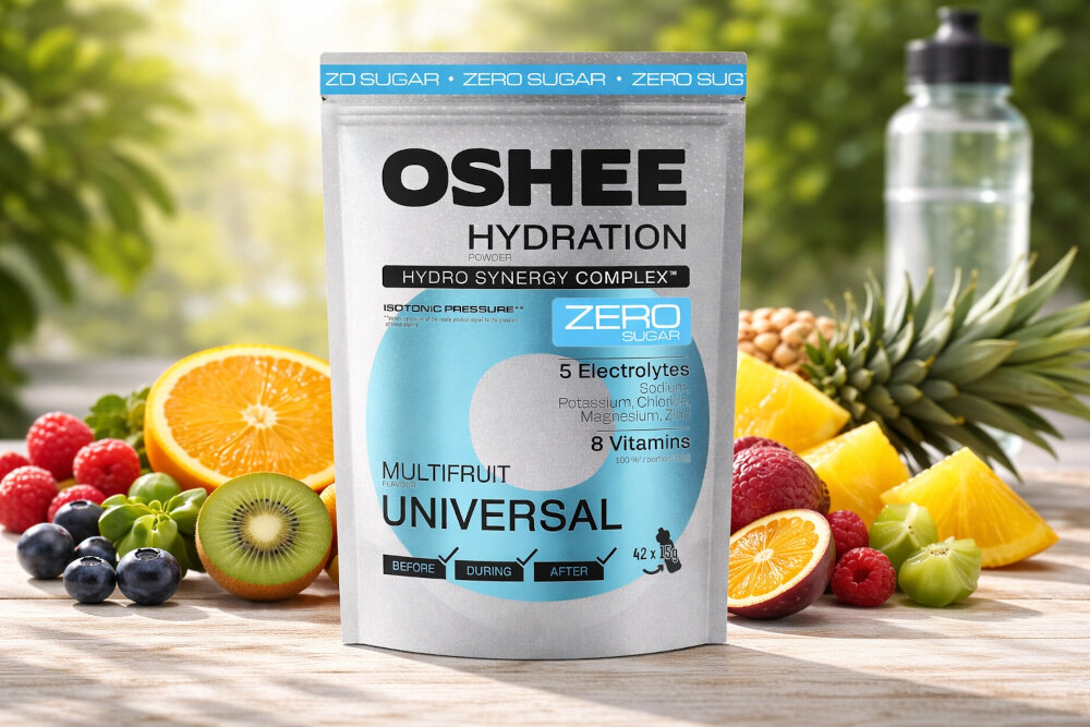 Izotonik OSHEE Hydration Zero Wieloowocowy (630 g) piasek opakowanie stoi na piasku wokół leżą różne owoce nawodnienie lekka formuła aktywność