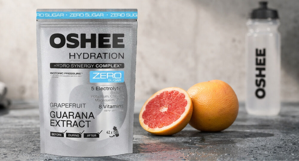 Izotonik OSHEE Hydration Zero Grejpfrutowy (630 g) siłownia podłoga na podłodze stoi opakowanie izotoniku obok leży pokrojony grejpfrut w tle bidon Hydro Synergy Complex™ OSHEE elektrolity wspierające prawidłową równowagę wodno-elektrolitową organizmu potas (2000 mg) magnez (400 mg) cynk (10 mg) w postaci diglicynianu cynku pomagają utrzymać prawidłową równowagę elektrolitową organizmu