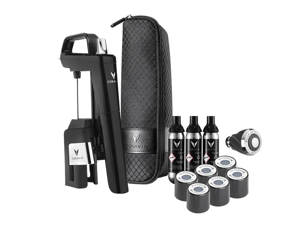 Na obrazie widoczny jest czarny system do przechowywania wina z logo CORAVIN, w zestawie z etui, czterema buteleczkami i kilkoma kapsułkami. Wszystkie elementy są ustawione na białym tle.