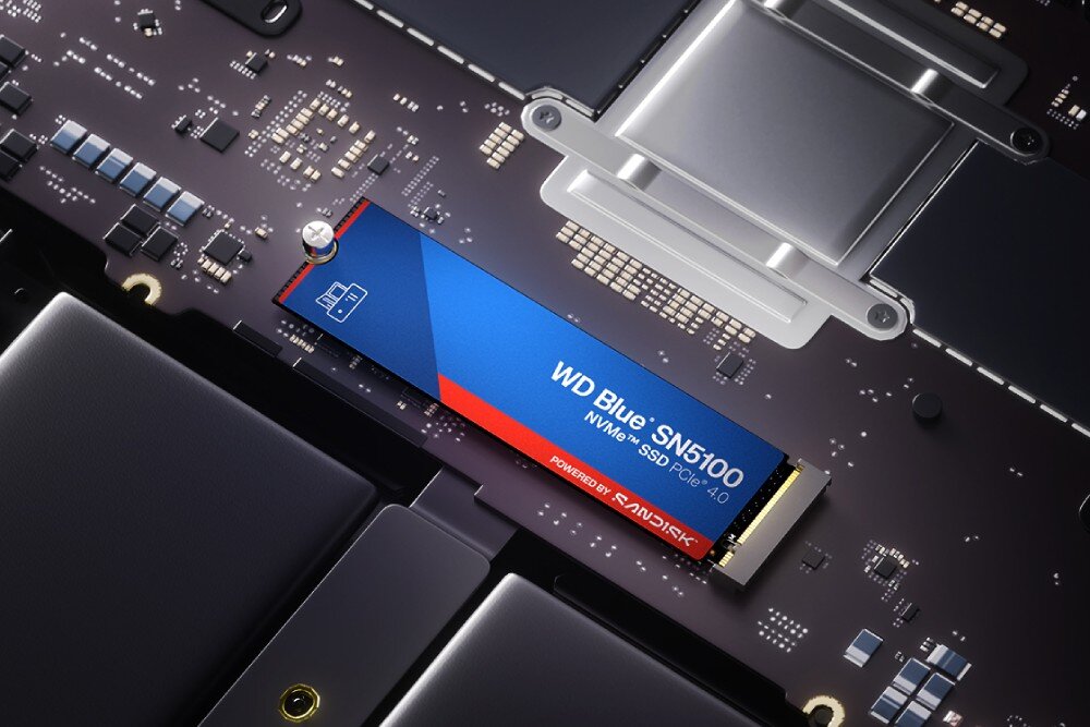Dysk SANDISK WD Blue SN5100 Dysk SSD M.2 zamontowany ukośnie na ciemnej płycie głównej komputera, przykręcony jedną śrubą po lewej stronie, widoczne ścieżki i małe układy scalone, opis