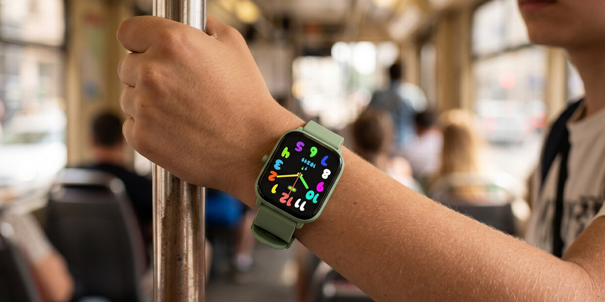 Osoba trzymająca się poręczy w tramwaju nosi zielony smartwatch z kolorowym wyświetlaczem, na którym widoczne są różnokolorowe cyfry i wskazówki zegara.